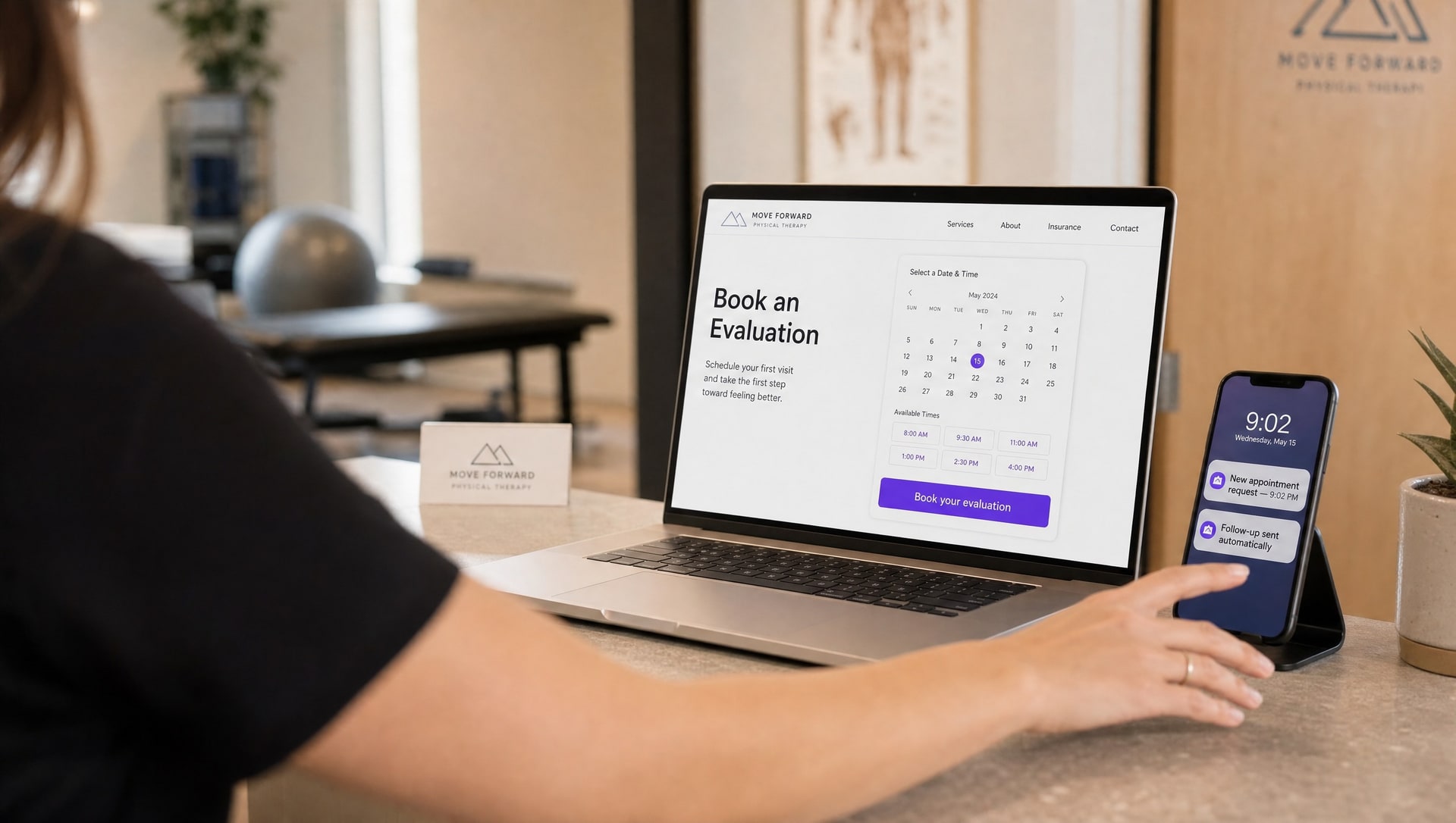 A physical therapist at a clinic reception desk reviewing new patient enquiries coming in on a screen.