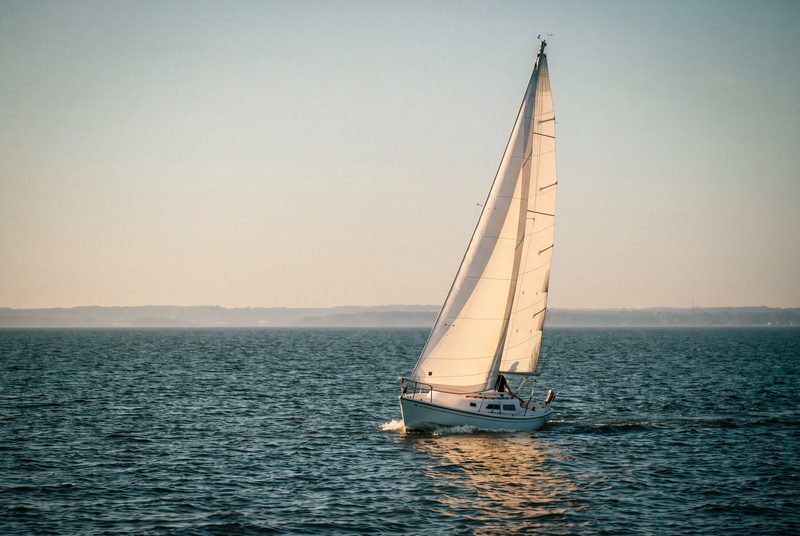 A single sloop under full sail heeling gently on a bay at sunset, the whole boat in frame.